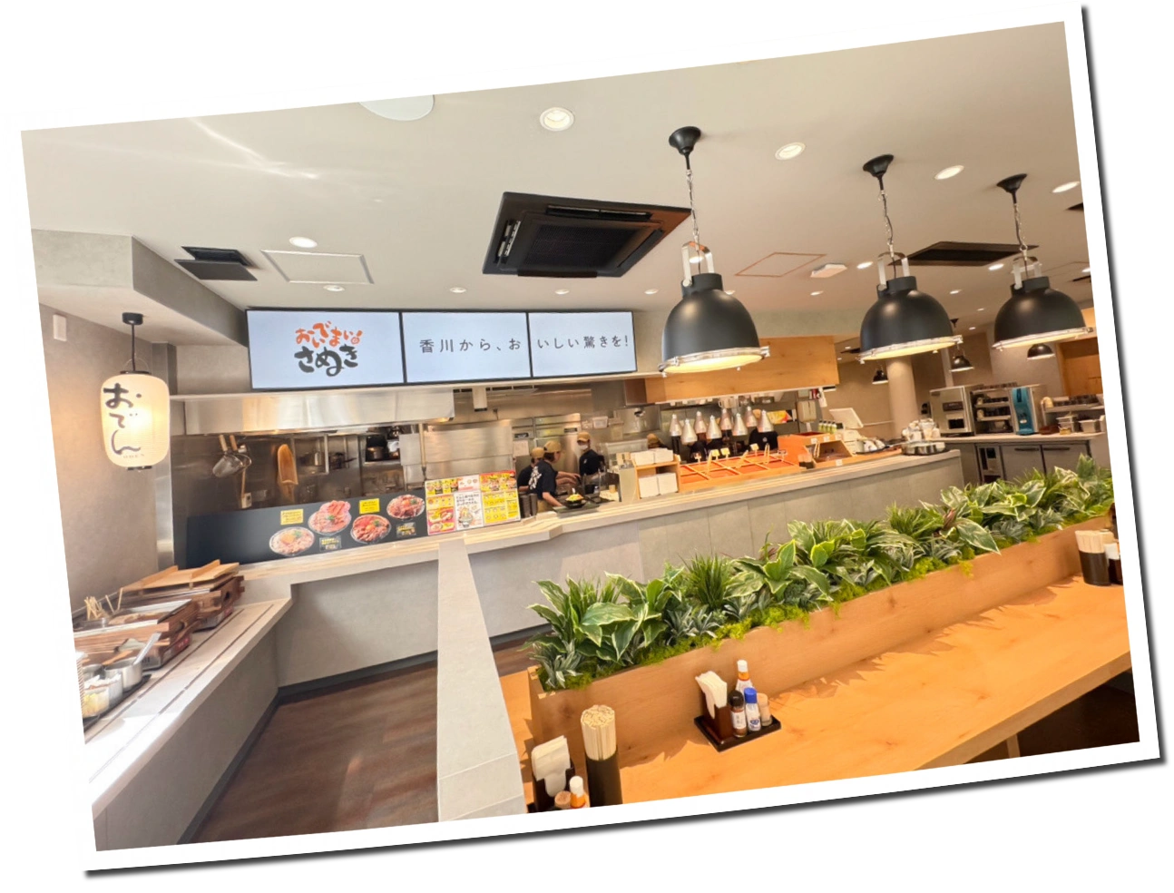 おいでまいさぬきの店内。カウンター席と厨房、メニューボードが見える様子。